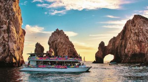 a small boat in a body of water with Arch of Cabo San Lucas in the background