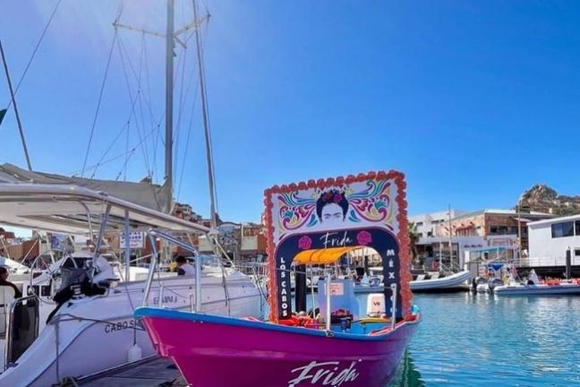 Colorful boat with Frida Kahlo portrait docked at a marina under a bright blue sky.