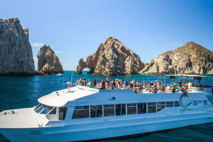 Tour boat with passengers in front of rocky arches on a sunny day.