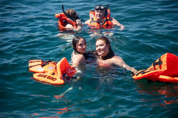 Four people in water wearing life vests, two smiling and two snorkeling.