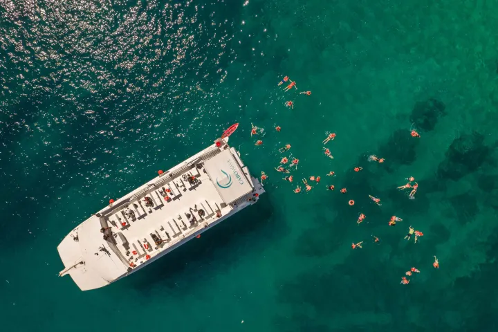 Aerial view of a boat on turquoise water with people swimming nearby.