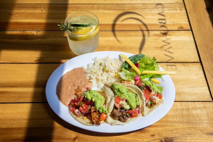 Plate with tacos, beans, rice, and salad on a wooden table, alongside a glass of lemon and cucumber drink.