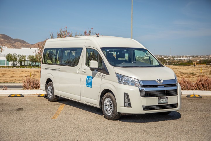 White passenger van parked outdoors on a sunny day with a desert landscape in the background.