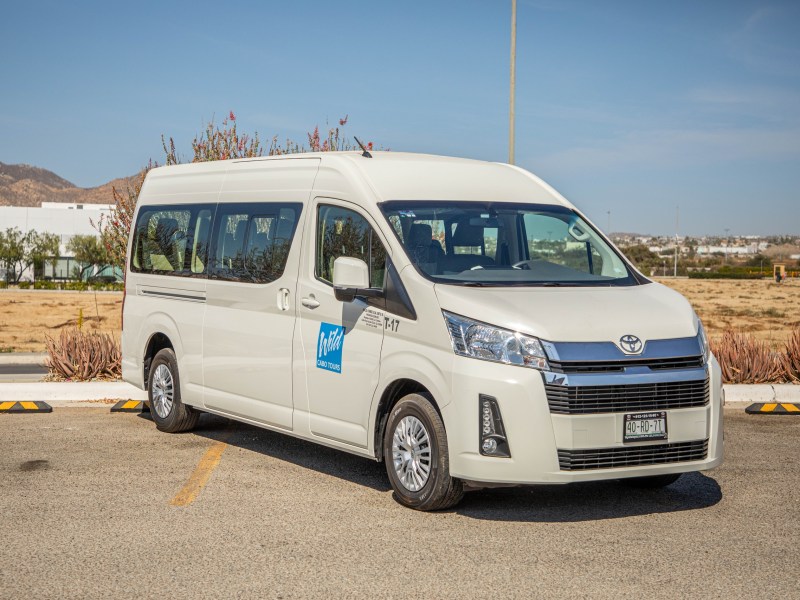 White passenger van parked outdoors on a sunny day with a desert landscape in the background.