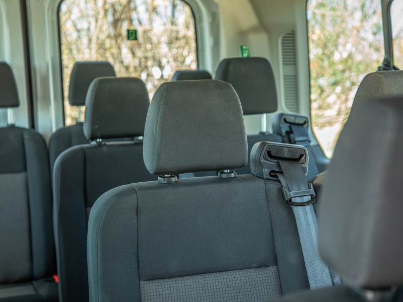 Interior of a van with multiple rows of empty gray seats and seatbelts.