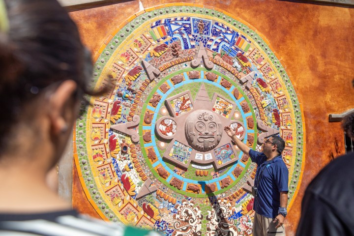 Tour guide explaining colorful circular mural to a group of people.