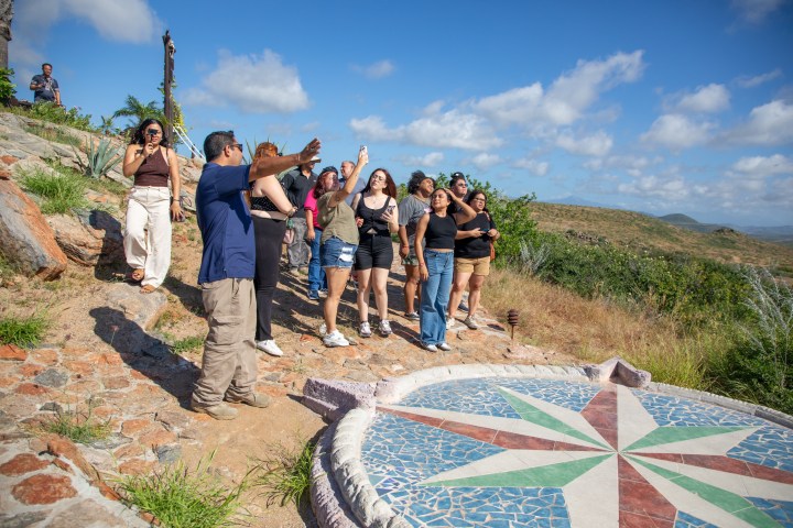 Group of people exploring a scenic outdoor area with a tiled compass on the ground.