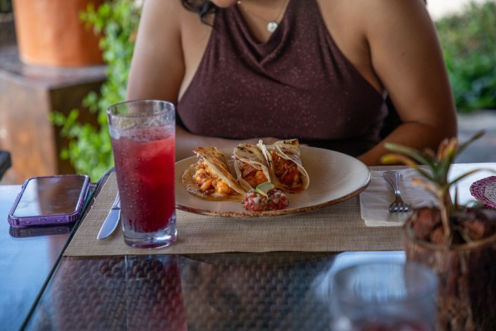Woman sitting at a table with tacos and a glass of red drink.