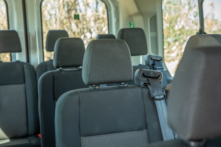 Interior of a vehicle showing empty gray fabric seats with headrests and seatbelts.