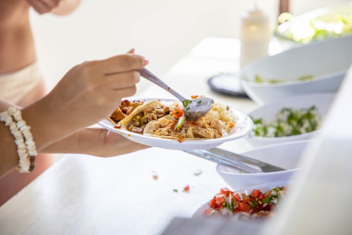 Person putting toppings on tacos from a buffet with various dishes.